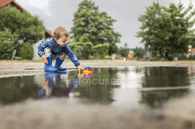 Kleiner blonder Junge in blauer Jacke und blauen Gummistiefeln — Stockfoto