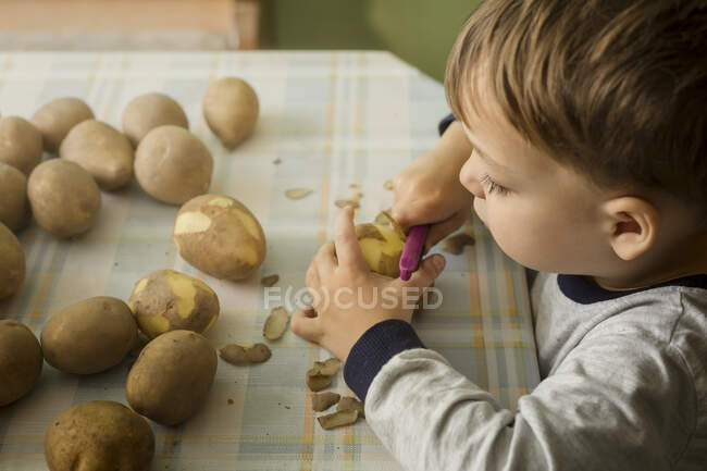 Bonito poy pilling potatoe em casa — Fotografia de Stock