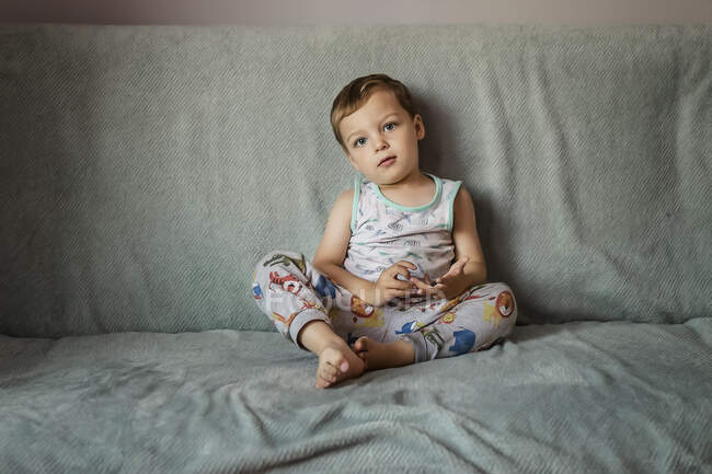 Loira menino pequeno com olhos azuis sentado no sofá dentro de casa — Fotografia de Stock