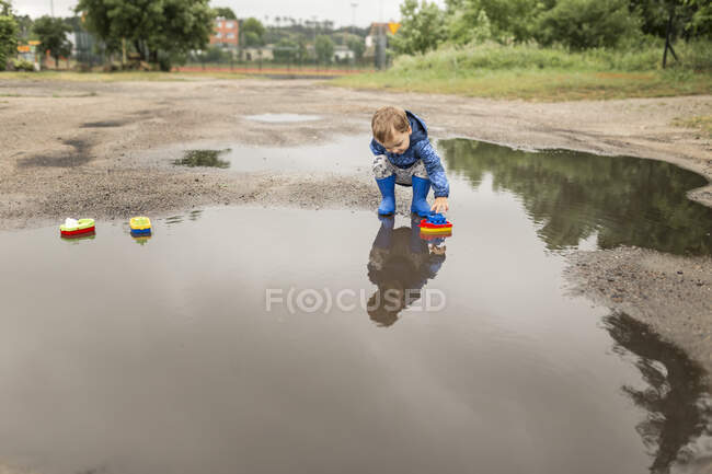 Kleiner blonder Junge in blauer Jacke und blauen Gummistiefeln — Stockfoto