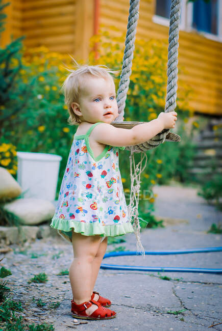 Menina bonito 3-4 anos de idade no jardim desempenha um balanço rústico — Fotografia de Stock
