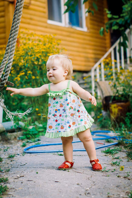 Cute baby girl 3-4 year old in the garden plays a rustic swing — Stock Photo