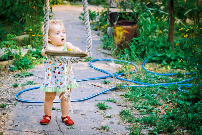 Симпатичная девочка 3-4 лет в саду играет на шуршащих качелях — стоковое фото