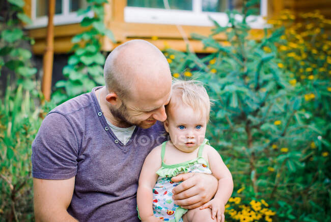 Padre sostiene a su hija en sus brazos en el jardín - foto de stock