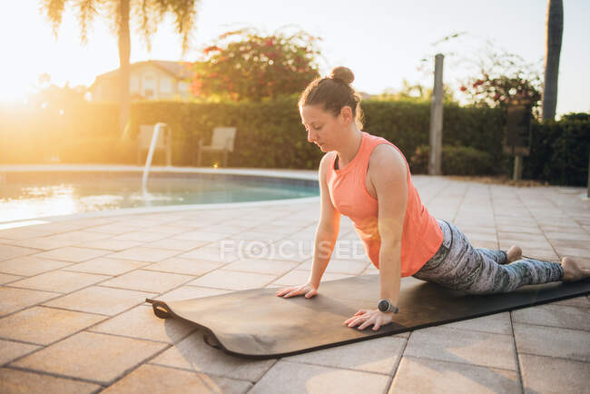 Uma mulher fazendo pilates, estendendo-se ao lado de uma piscina ao nascer do sol — Fotografia de Stock