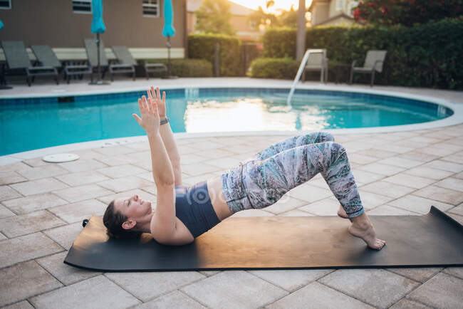 A woman doing mat pilates & glute bridges next to a pool at sunrise — Stock Photo