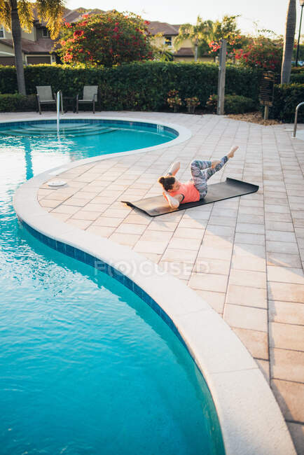 Una donna che fa pilates mat & crunches accanto a una piscina all'alba — Foto stock