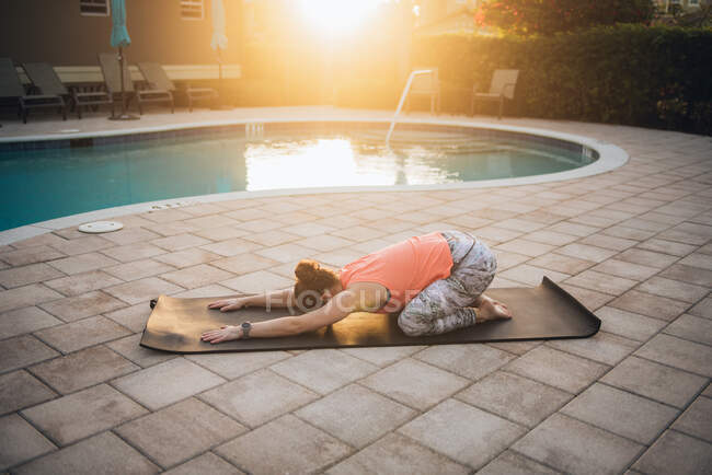 A woman doing mat pilates & stretching next to a pool at sunrise — Stock Photo