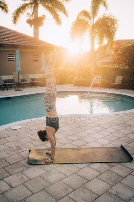 A woman doing a handstand & mat pilates next to a pool at sunrise — Stock Photo