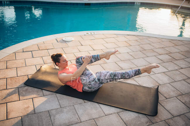 Uma mulher fazendo pilates esteira ao lado de uma piscina ao nascer do sol no verão — Fotografia de Stock