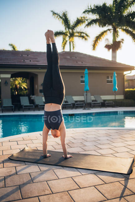 Uma mulher fazendo esteira pilates & um suporte de mão ao lado de uma piscina ao nascer do sol — Fotografia de Stock