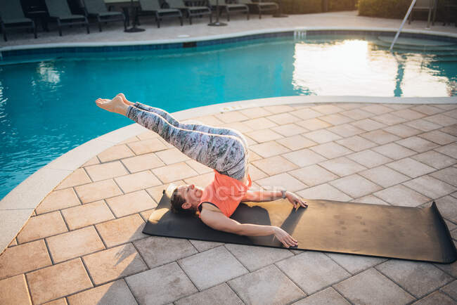 Uma mulher fazendo pilates esteira ao lado de uma piscina ao nascer do sol no verão — Fotografia de Stock