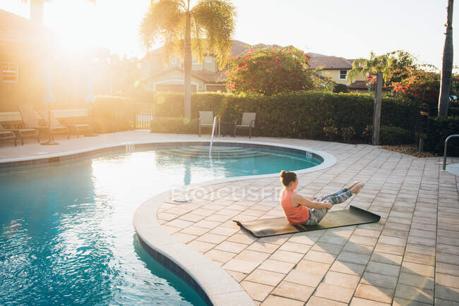 Eine Frau pilatet im Sommer neben einem Pool bei Sonnenaufgang — Stockfoto