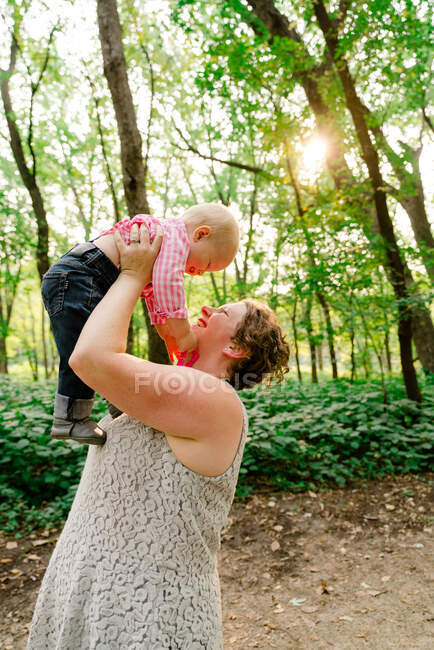Side view of a mother lifting her baby boy in the air — Stock Photo