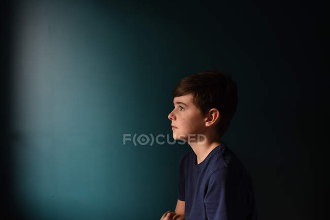 Portrait of a sad young boy against a dark blue wall. — Stock Photo