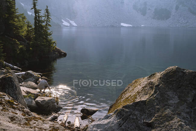 Wanderin sammelt Wasser in einem unberührten Bergsee, um es zu filtern — Stockfoto