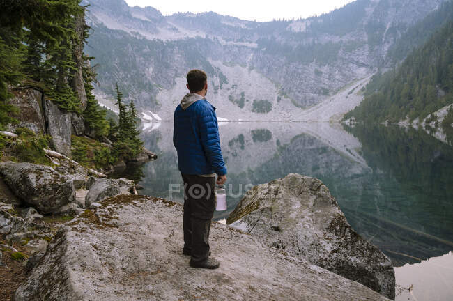 Мужчина в голубой пушистой куртке стоит рядом с чистым озером — стоковое фото