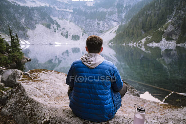 Masculino sentado ao lado do lago alpino azul nas cascatas — Fotografia de Stock