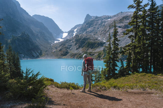 Female with backpack standing next to gorgeous alpine lake — Stock Photo