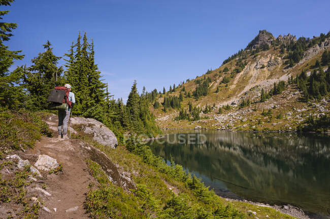 Feminino com mochila em pé ao lado do lago alpino nas cascatas — Fotografia de Stock