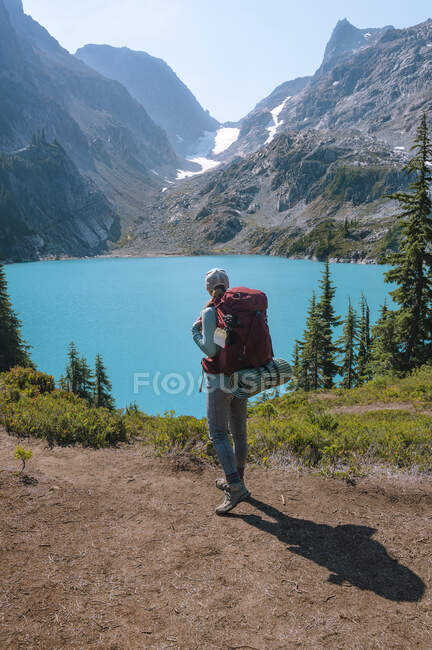 Жінка з рюкзаком стоїть поруч з дивовижним синім кольоровим альпійським озером — стокове фото