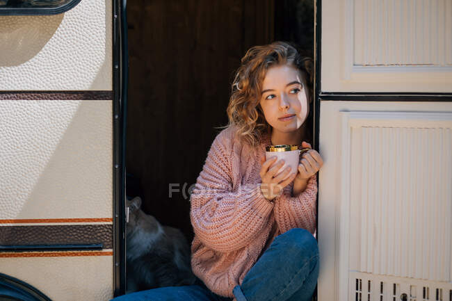 Mulher bebendo café com gato na porta do reboque. — Fotografia de Stock