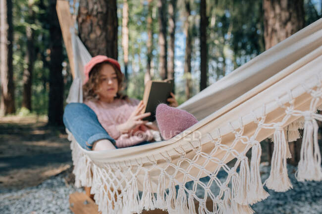 Mulher em rede leitura livro na floresta. — Fotografia de Stock