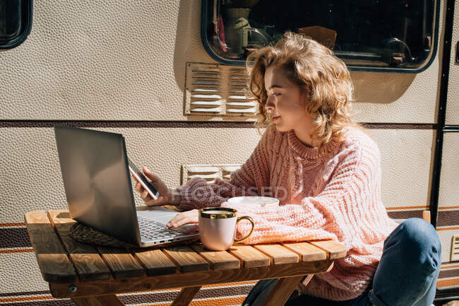 Жінка в ноутбуці з телефоном, що працює біля трейлера . — стокове фото