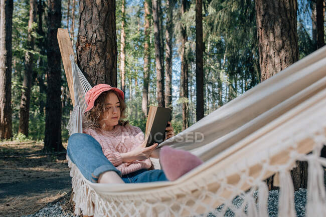 Jovem mulher em rede leitura livro na floresta. — Fotografia de Stock