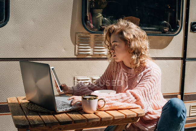 Женщина за ноутбуком с телефоном рядом с трейлером. — стоковое фото