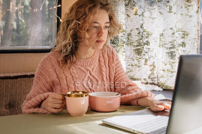 Frau im Wohnwagen frühstückt am Laptop. — Stockfoto