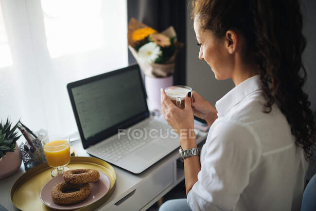 Woman looking at he laptop and smiling while holding a cup of co — Stock Photo