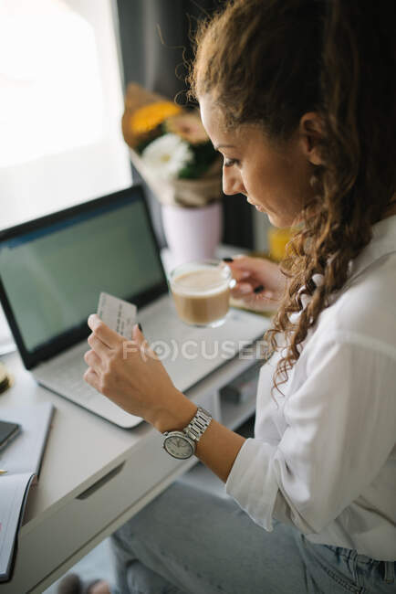 Femme assise à son bureau et regardant sa carte de crédit — Photo de stock