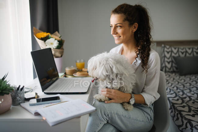 Mulher sentada em sua mesa com um cão em seu colo. — Fotografia de Stock