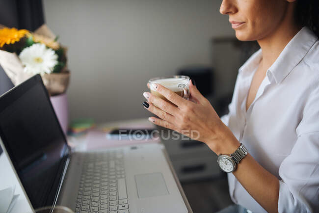 Frau sitzt mit einer Tasse Kaffee vor einem Laptop. — Stockfoto