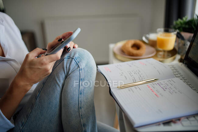 Close-up of a woman looking at her phone with a notebook and pen — Stock Photo