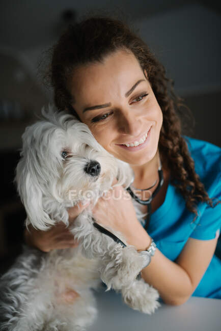 Veterinário sorrindo enquanto se abraça com um cão. — Fotografia de Stock