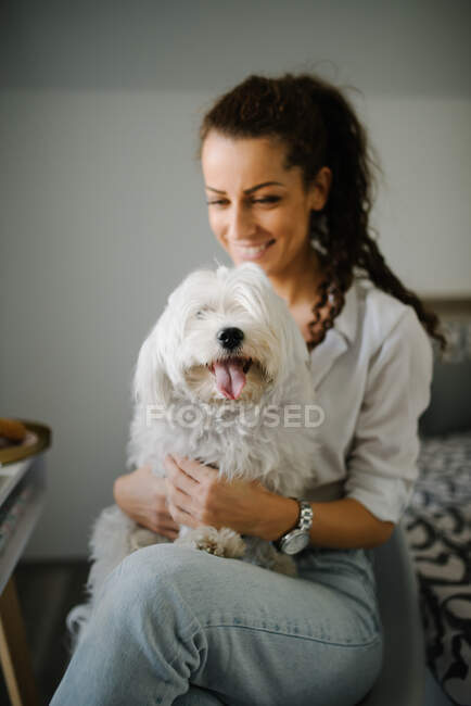 Mulher sentada em uma cadeira com um cão no colo e sorrindo. — Fotografia de Stock