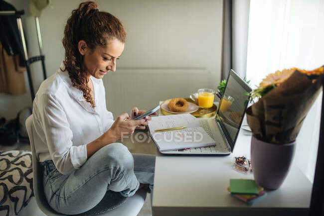 Mulher sentada na mesa, olhando para o telefone e sorrindo. — Fotografia de Stock