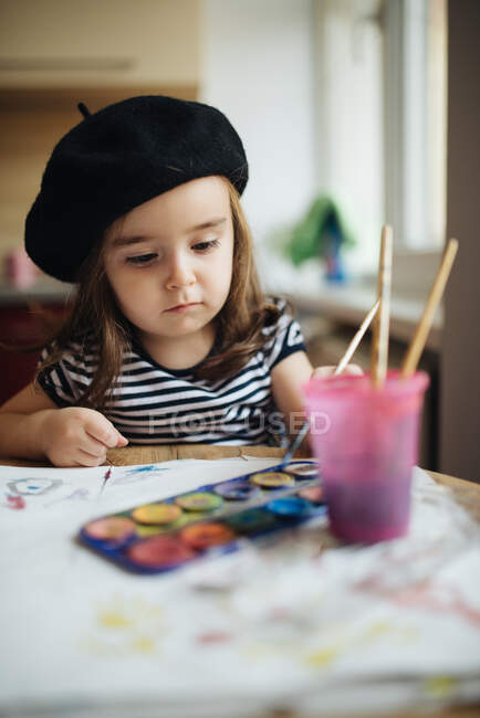 Junges Mädchen mit schwarzer Baskenmütze sitzt an einem Küchentisch und — Stockfoto