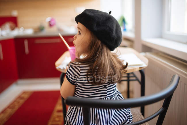 Молода дівчина з чорним беретом сидить за кухонним столом . — стокове фото
