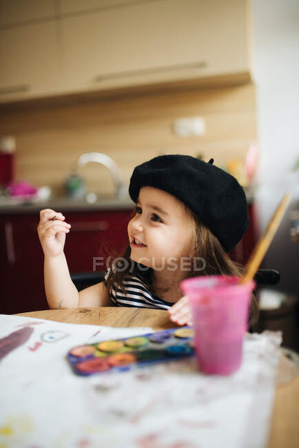 Young girl with a black beret drawing in the kitchen. — Stock Photo