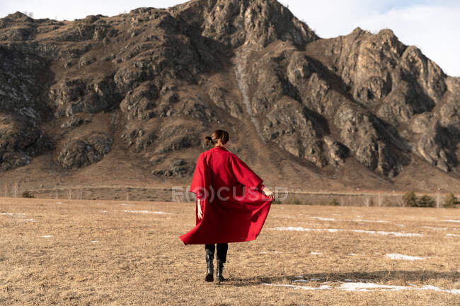 Жінка ззаду в червоному пальто біжить біля гори — стокове фото