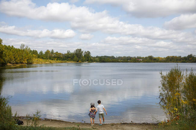 Two small children stand by lake on sunny summer day — Stock Photo
