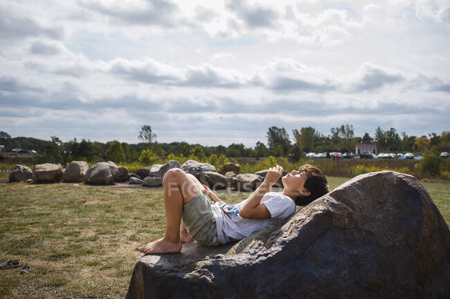 A tween boy lays happily on big rock in warm sunshine — Stock Photo