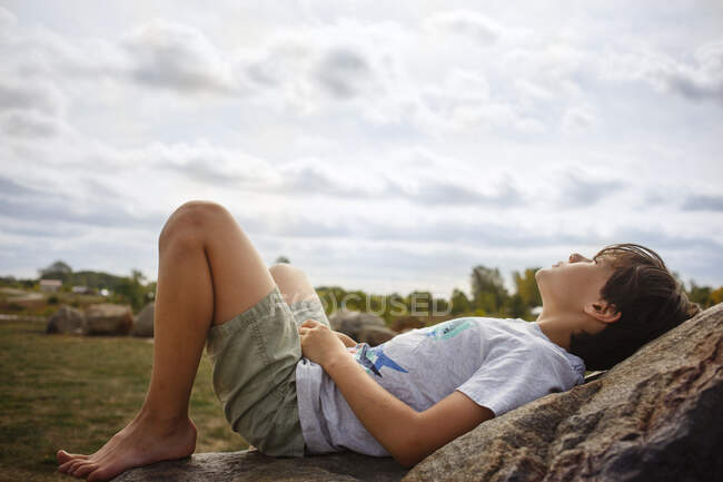 Маленький мальчик лежит на скале босиком на солнце — стоковое фото