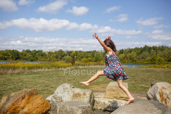 A little barefoot child leaps across large boulders outside — Stock Photo