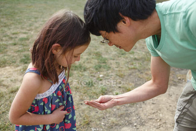 Ein Vater und ein kleines Mädchen schauen sich etwas in seinen Händen genau an — Stockfoto