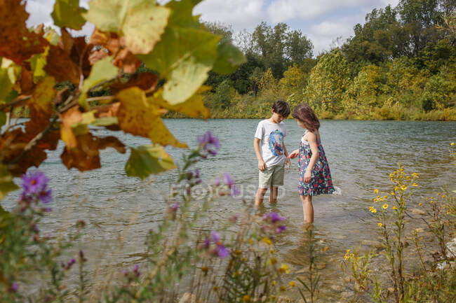 Un bambino e una bambina stanno insieme a guadare in un lago in estate — Foto stock