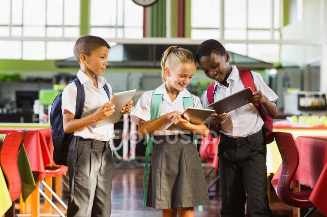 Niños en edad escolar usando tableta digital en cafetería escolar - foto de stock